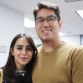Two students pose together for a photo in a classroom setting, with other participants and training materials visible in the background.