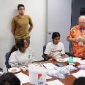 Instructor standing at a table demonstrating a hands-on clinical skill with training materials while students seated around observe and follow along.