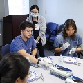 Students seated around a table working with small medical tools and components during a hands-on clinical training session in a classroom.