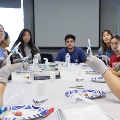 Students gathered around a large table using syringes and training materials during a collaborative medical skills workshop.